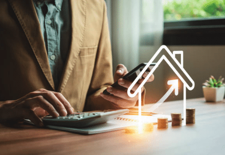Person using calculator and phone beside stacked coins with rising property icon overlay